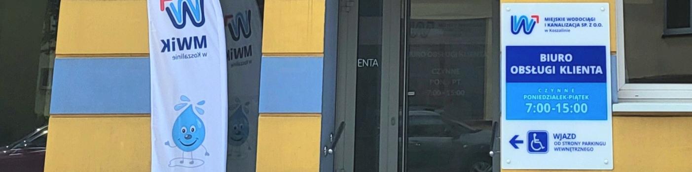 Wejście do budynku Biura Obsługi Klienta MWiK, obok biało niebieska flaga reklamowa